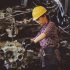 woman wears yellow hard hat holding vehicle part