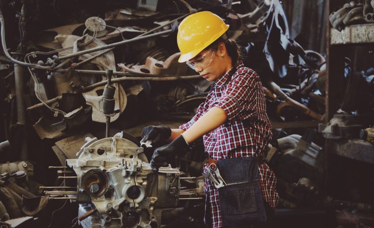 woman wears yellow hard hat holding vehicle part