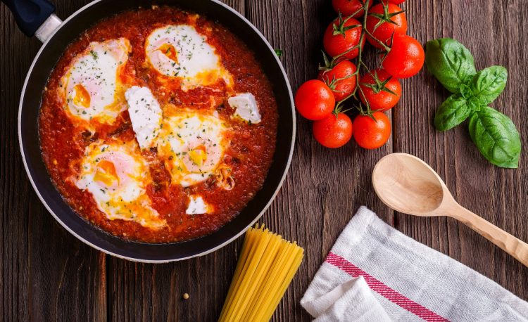 black frying pan with spaghetti sauce near brown wooden ladle and ripe tomatoes