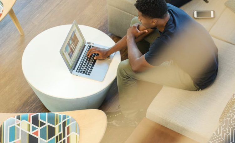 man using gray laptop while sitting on beige sofa