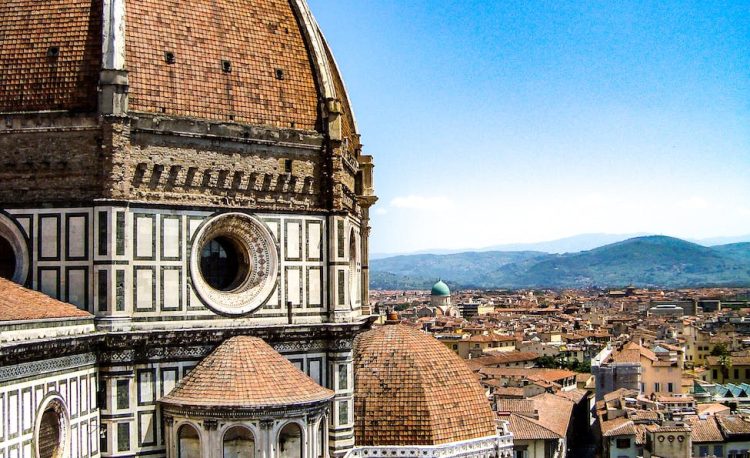 brown and white painted cathedral roof overlooking city and mountain under blue sky