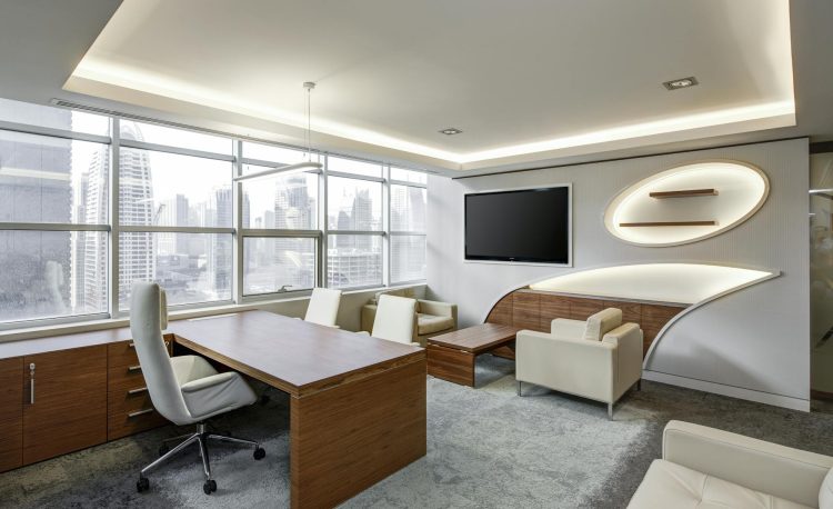 gray office rolling chair near brown wooden desk in front of flat screen tv on white painted wall