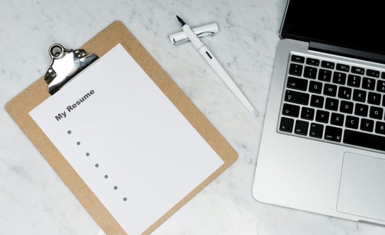 a clipboard near pen and laptop on a marble surface