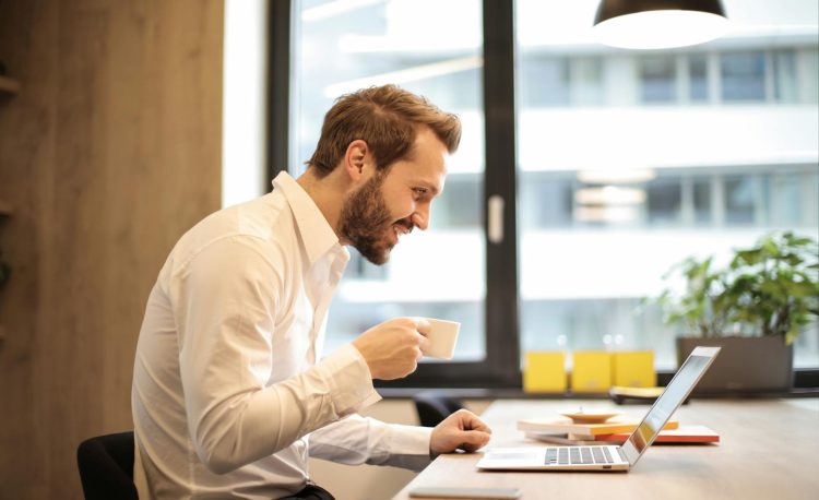 man holding teacup infront of laptop on top of table inside the room