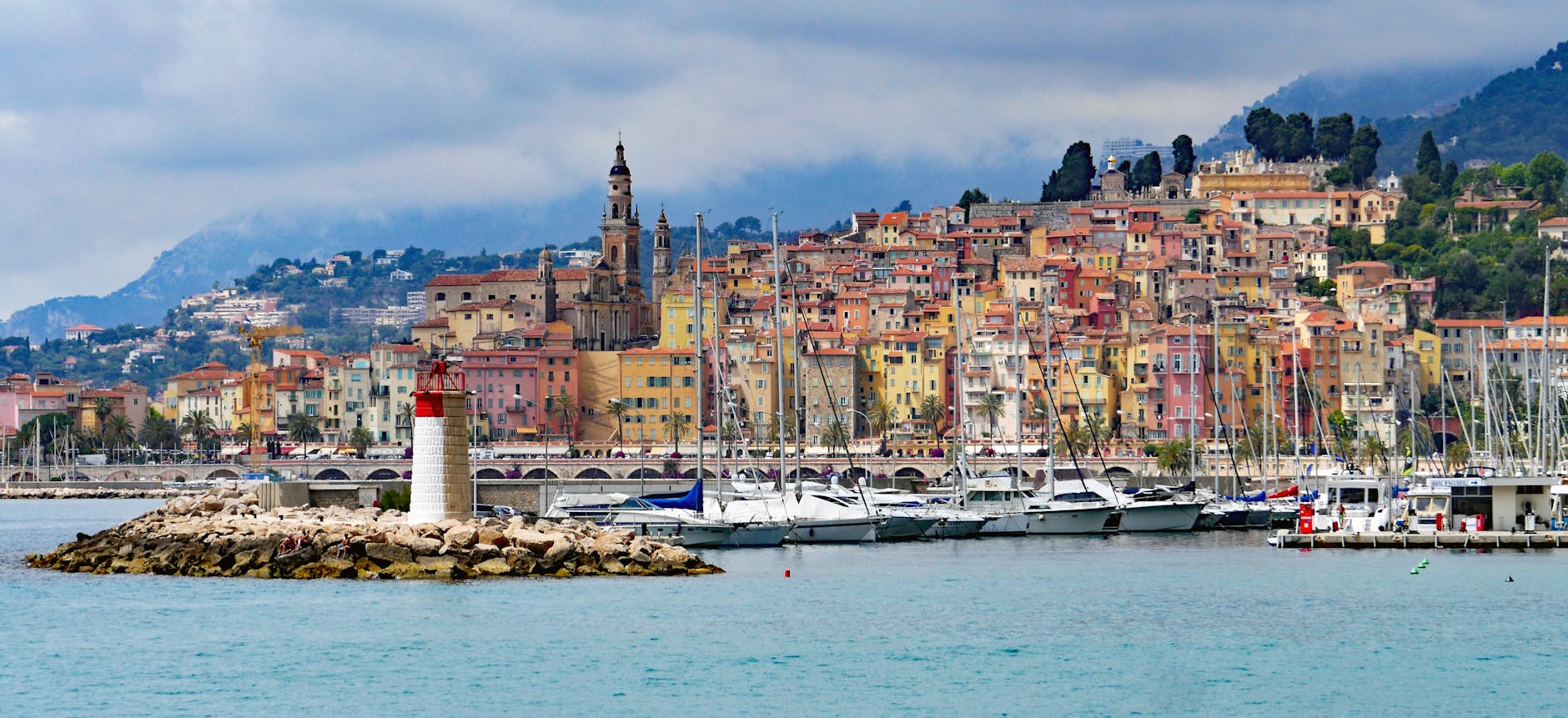 houses near with sea with sailboats and lighthouse during daytime